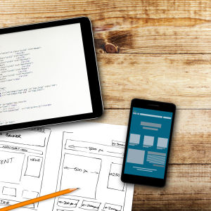 website wireframe sketch and programming code on digital tablet